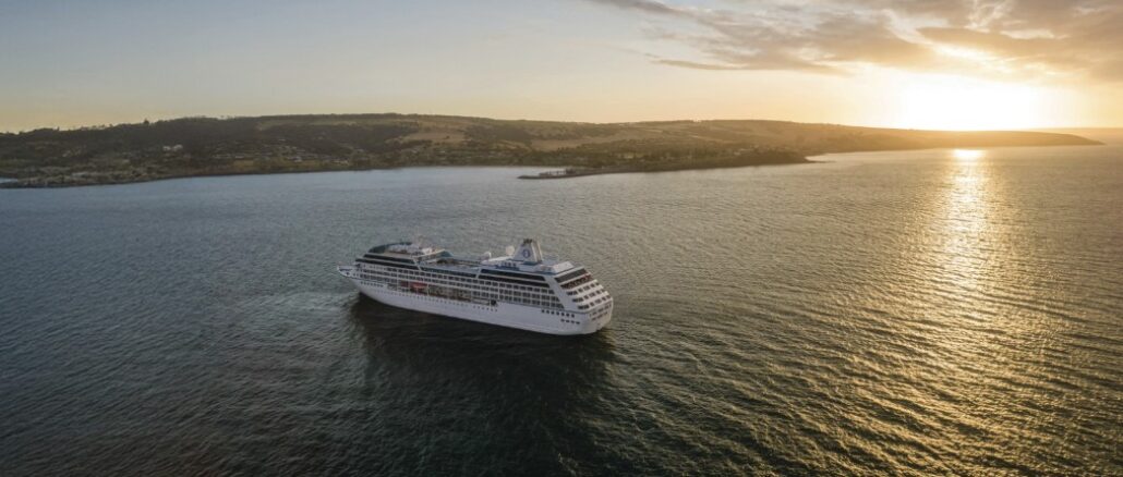White cruise ship sailing on calm sea at sunset, coastline visible in the distance.
