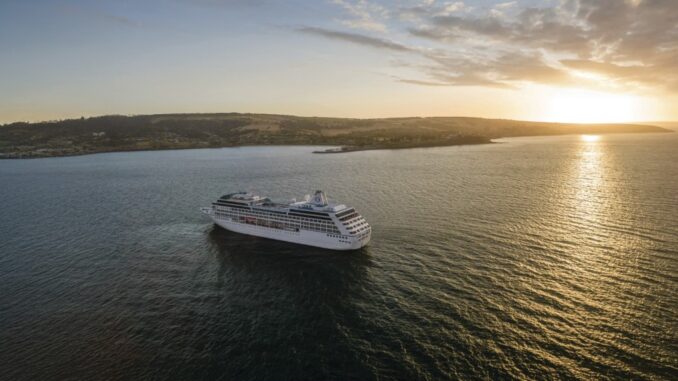 White cruise ship sailing on calm sea at sunset, coastline visible in the distance.