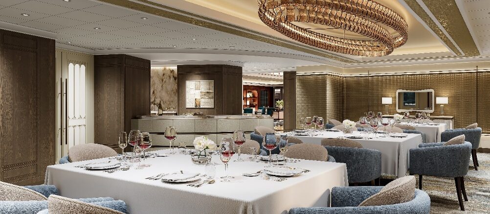 Elegant hotel dining room with white-tablecloth tables, blue upholstered chairs, and a large circular crystal chandelier overhead.