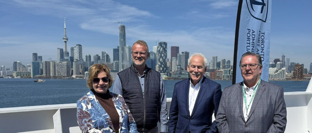 Four adults posing on a boat deck with Toronto's skyline and the CN Tower in the background on a sunny day.