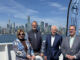 Four adults posing on a boat deck with Toronto's skyline and the CN Tower in the background on a sunny day.