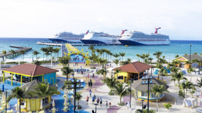 Two large cruise ships docked offshore as a sunny tropical port comes to life with palm trees and colorful buildings along a promenade.