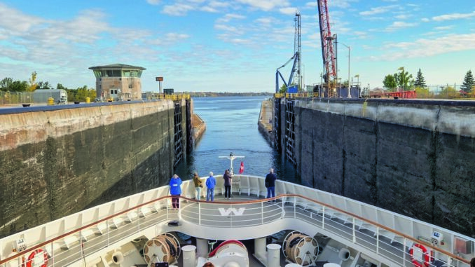 Cruise ship entering a canal lock, with tall concrete walls and cranes on the sides under a blue sky.