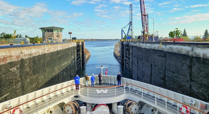 Cruise ship entering a canal lock, with tall concrete walls and cranes on the sides under a blue sky.