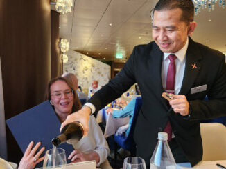 A waiter in a suit pours wine into a glass for a smiling woman at a table during a formal event.