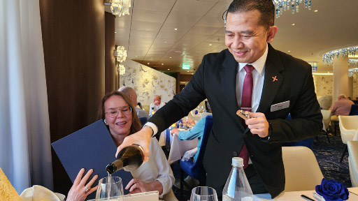 A waiter in a suit pours wine into a glass for a smiling woman at a table during a formal event.