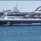 Large white and navy cruise ship docked at a port, with orange lifeboats along its side.