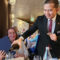 A waiter in a suit pours wine into a glass for a smiling woman at a table during a formal event.